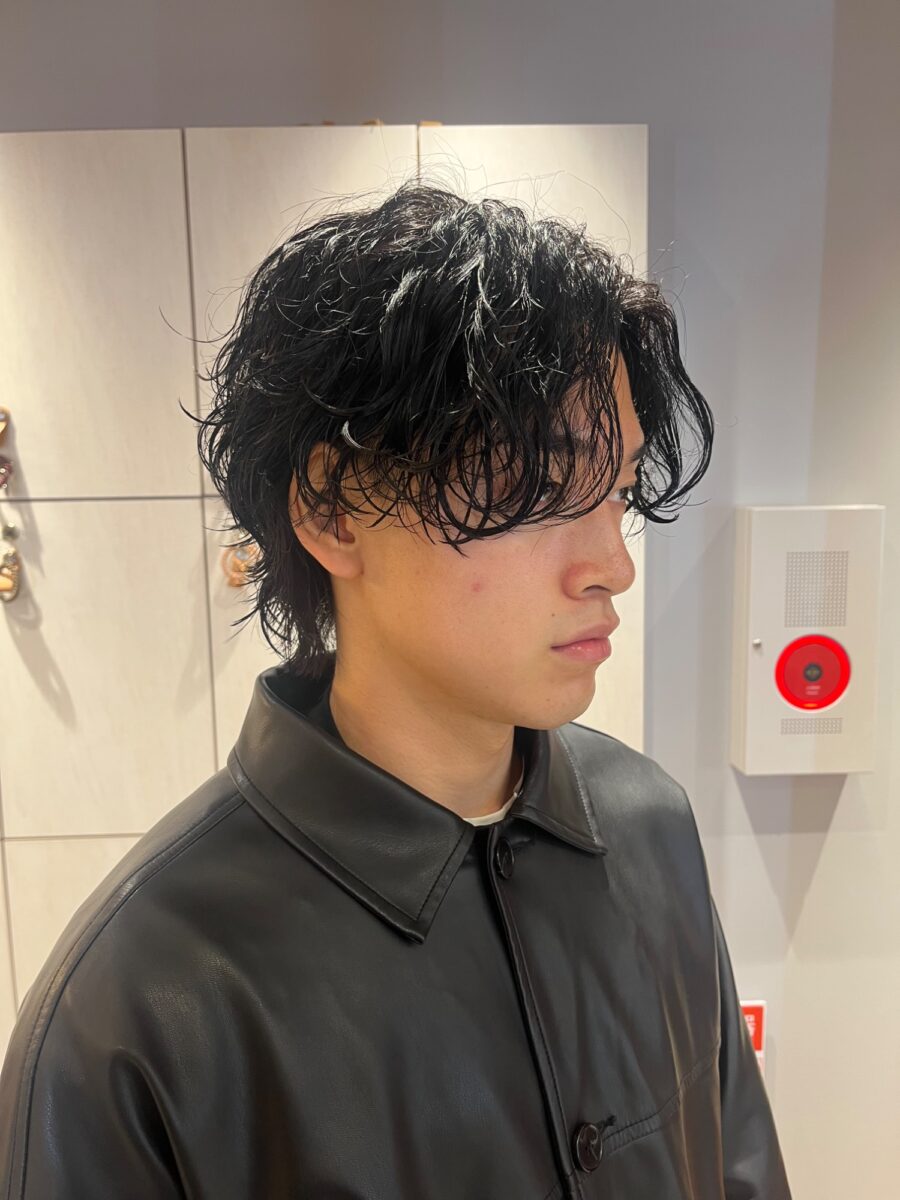 黒髪に無造作なウェーブを効かせたメンズパーマの横顔スタイル